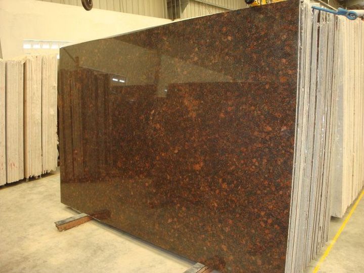 Polished brown and black granite slab standing in a warehouse